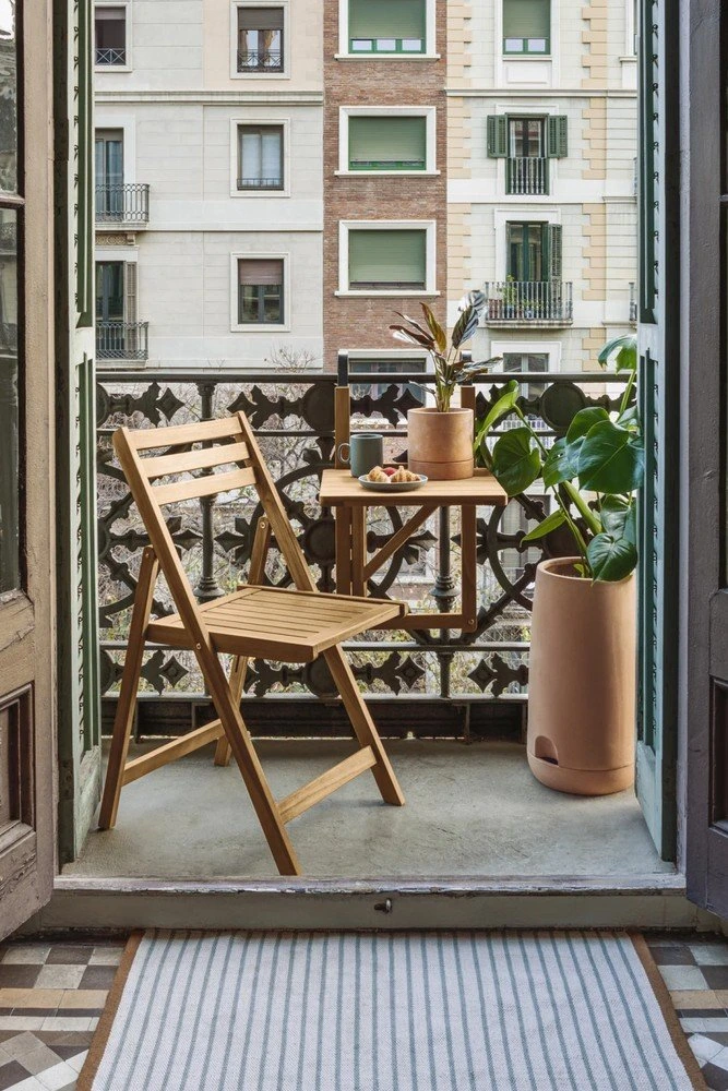 Malý balkon s dřevěnou židlí, stolem a květinami v nádobách.