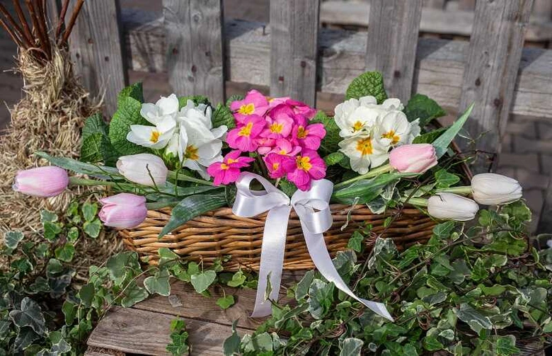 Květinová kytice s narcisy a tulipány v košíku na dřevěném povrchu.
