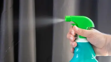 Ruka stříká tekutinu z rozprašovače před tmavými závěsy.