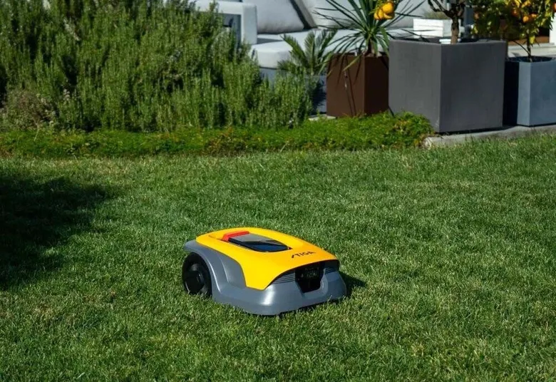 Autonomní robota sekačka na trávu pracuje v zahradě.