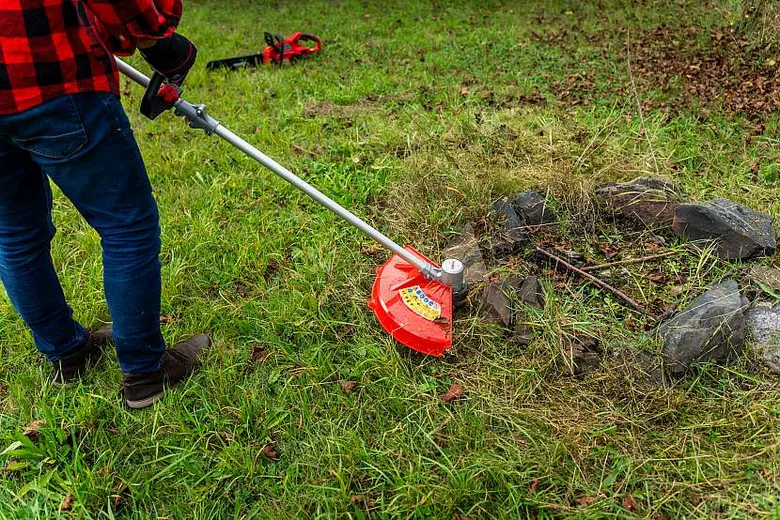Osoba seřezává trávu kolem kamenů motykou na zahradě.