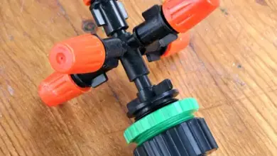 Černý postřikovač s oranžovými víčky na dřevě.