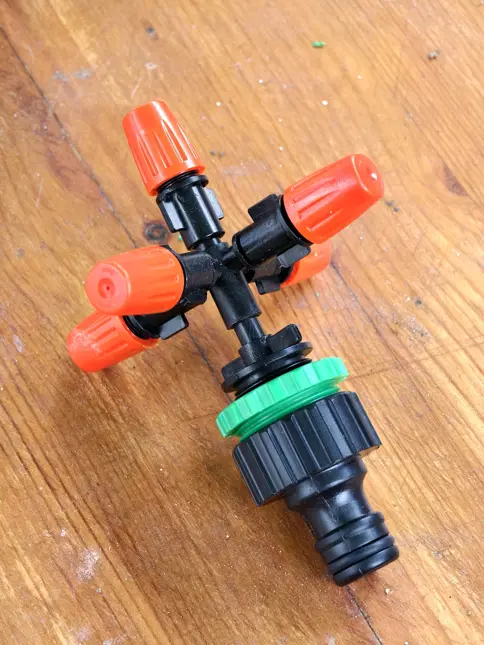 Černý postřikovač s oranžovými víčky na dřevě.
