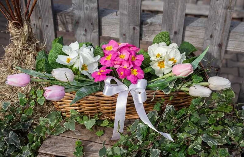 Koš s růžovými tulipány, bílými květy a stříbrnou stuhou na dřevěném povrchu.